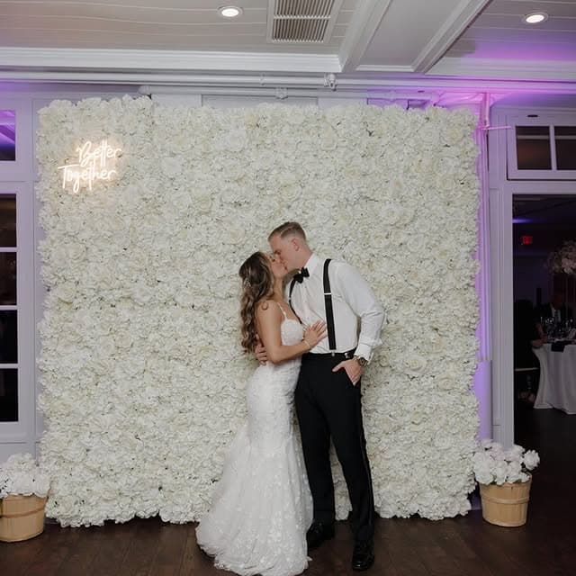 Bride and groom kissing in front of a white flower wall